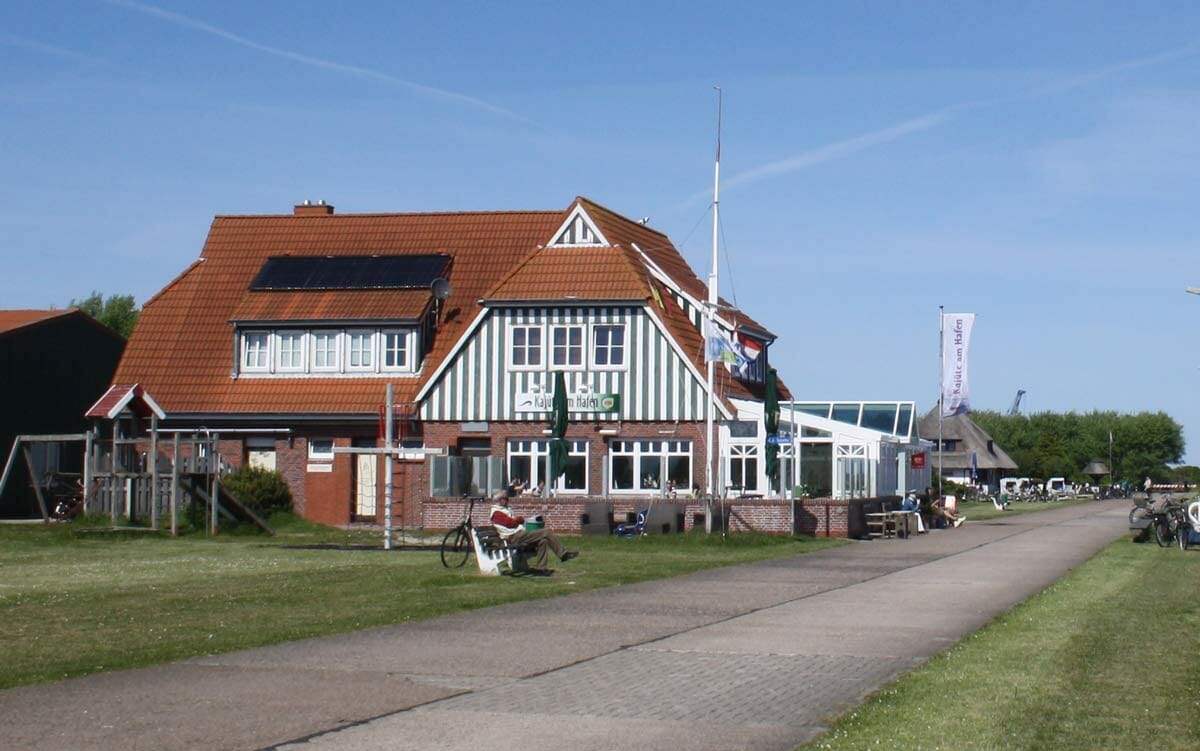 Straße auf einem Deich mit Restaurant links und dem Hafen rechts