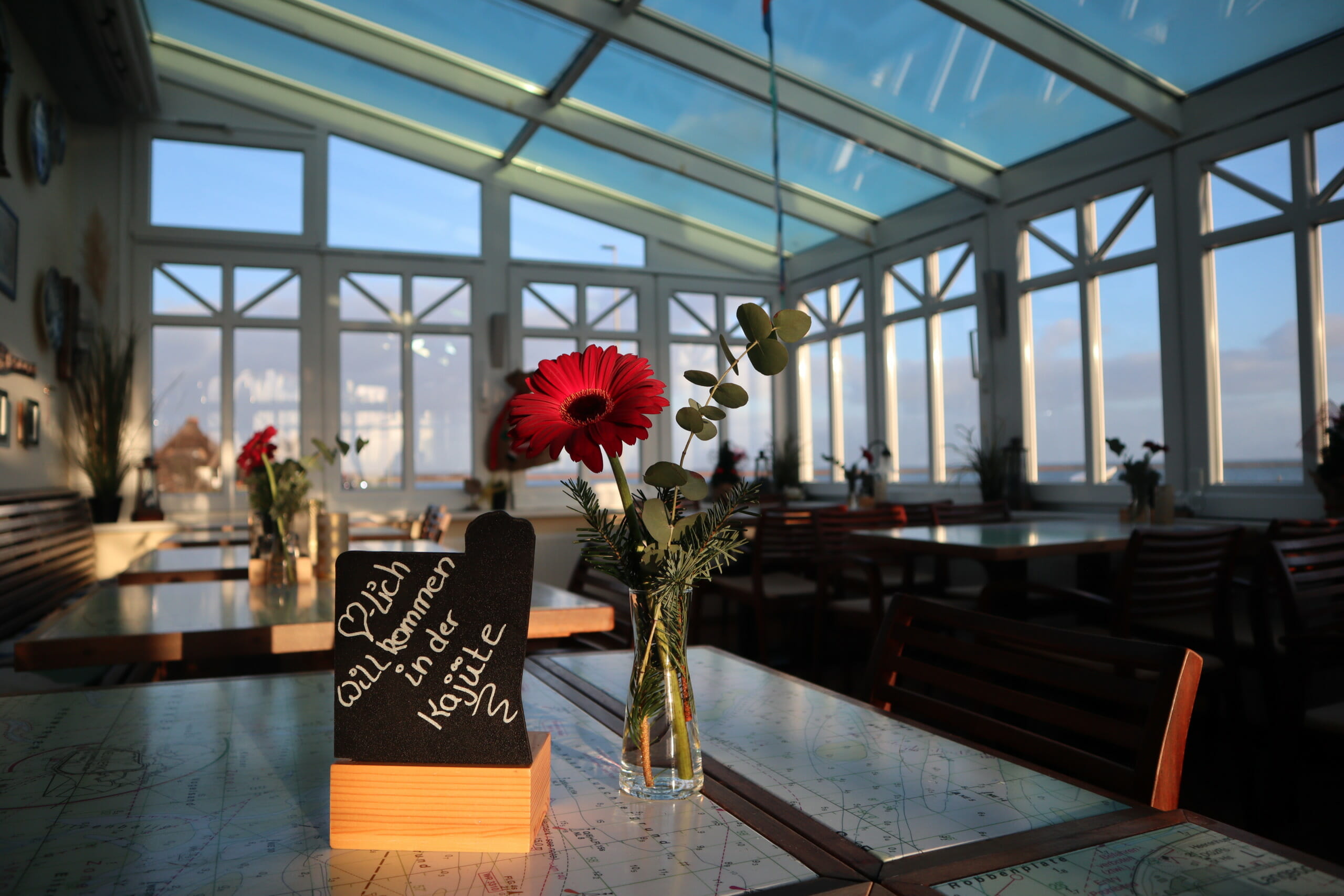 Ein Tisch mit einer Blumen in einer Vase. Der Tisch steht in einem Wintergarten in einem Restaurant.